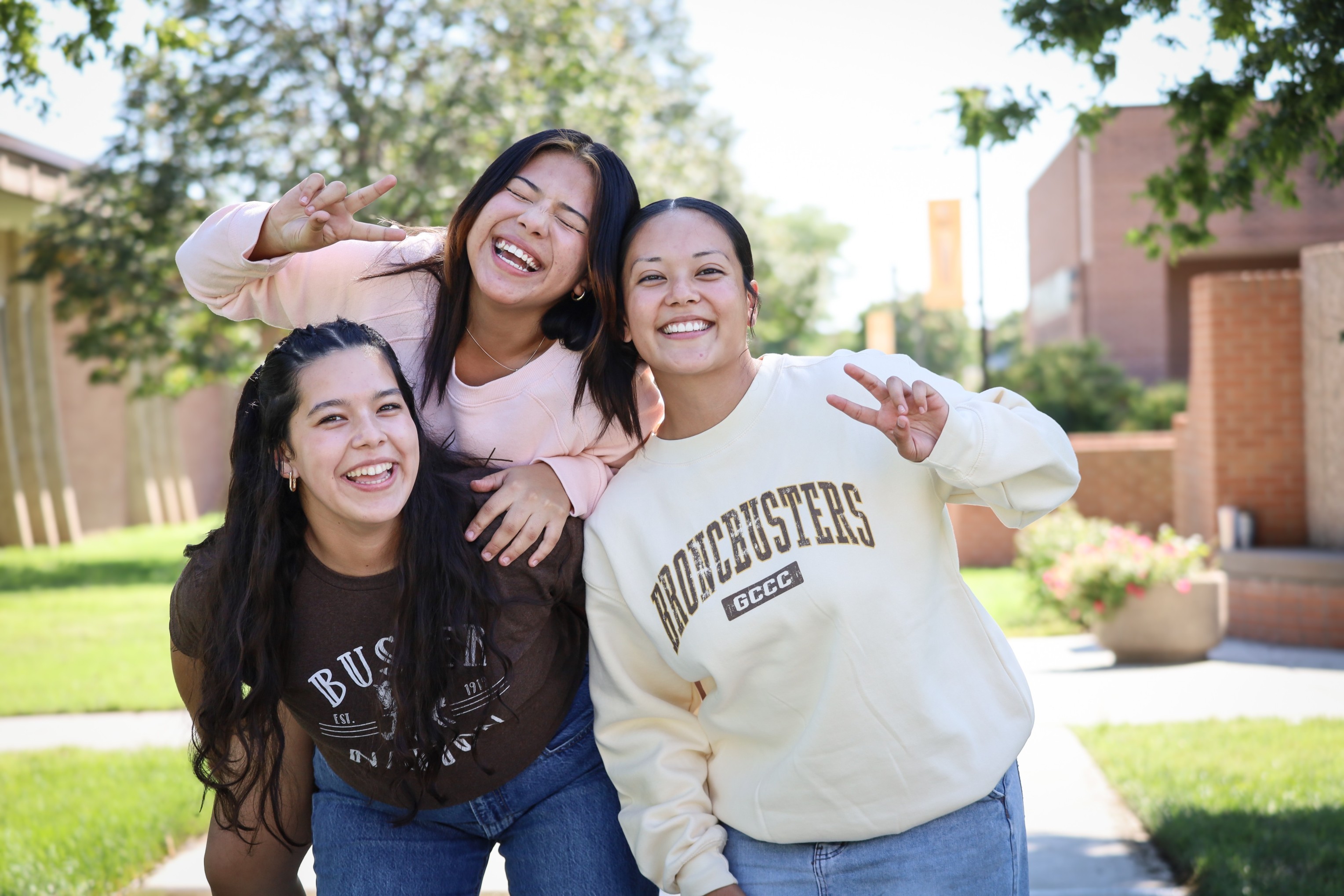 Three college students standing together on campus outdoors, posing for a photo.