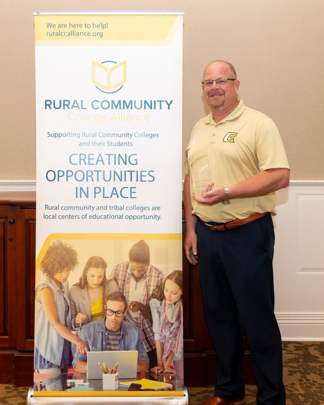 Man standing next to a banner promoting rural community colleges and educational opportunities in local places.
