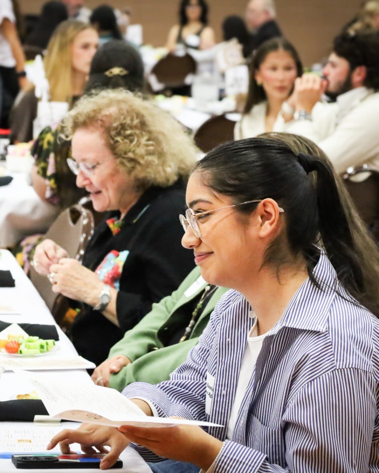 Attendees seated at banquet tables review event materials during a scholarship celebration program.