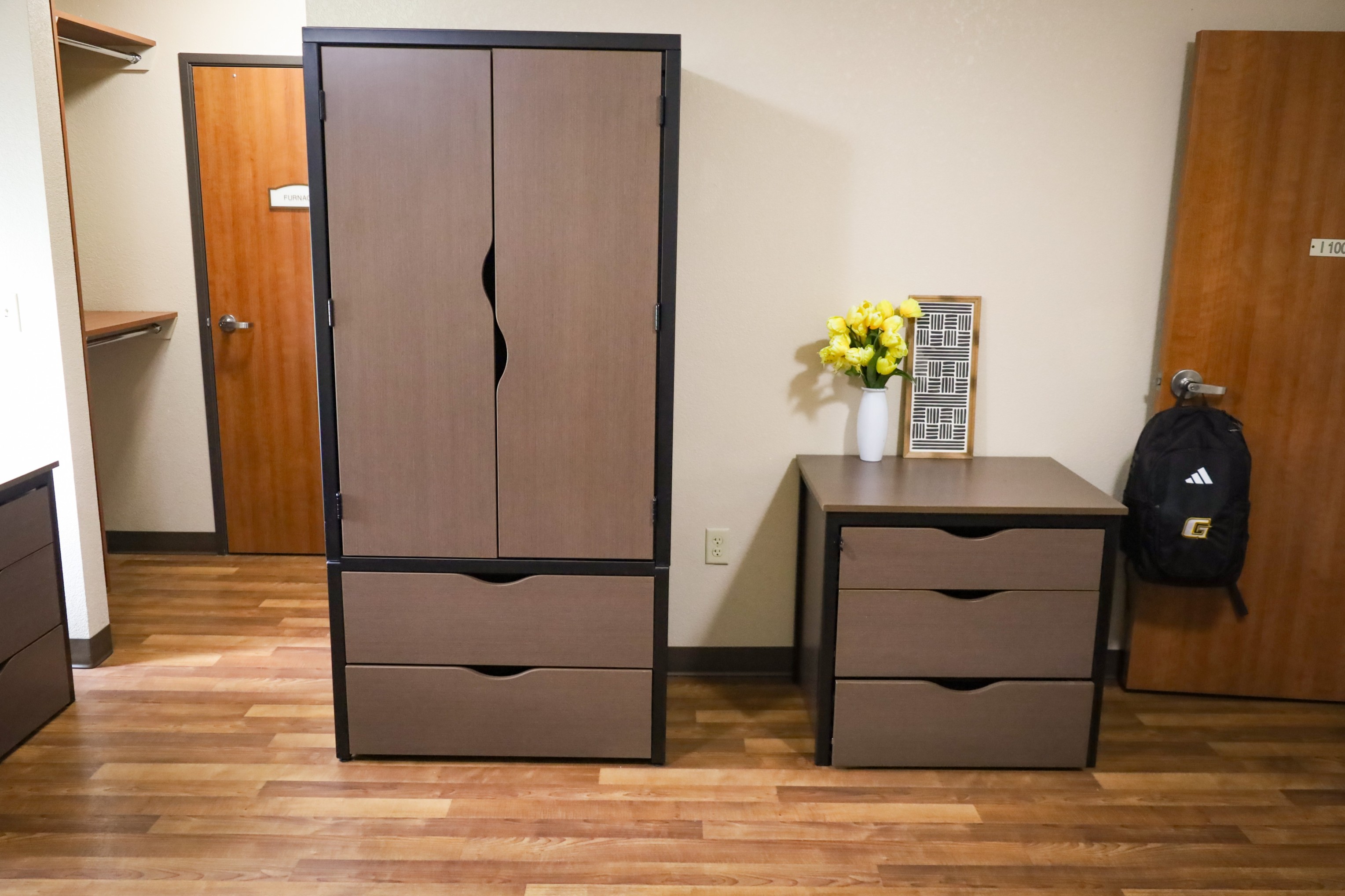 Bedroom with wardrobe closet, drawer unit, and small dresser with flowers next to a door.